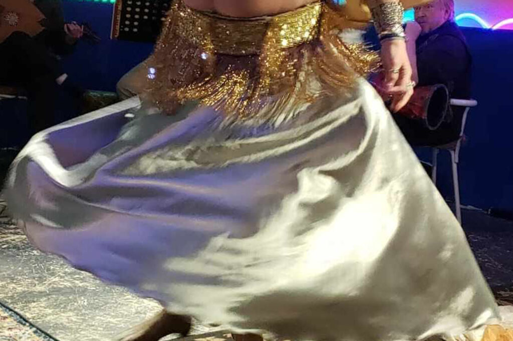 A bellydancer wearing a white skirt and a gold top.